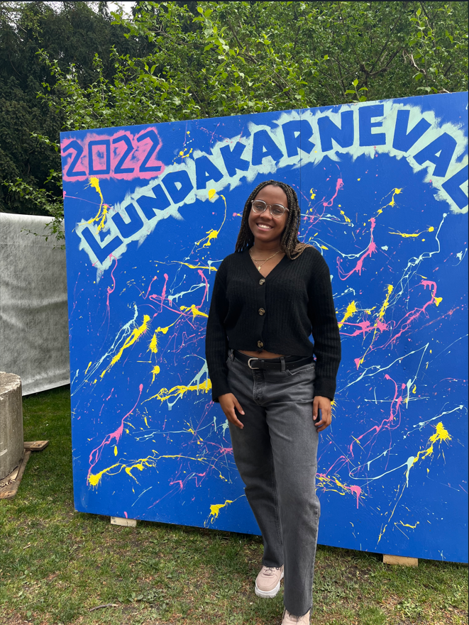 Student intern Bethany Bazemore in front of a large blue sign with paint splattered on it